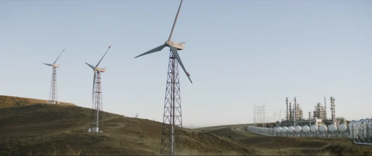 Aerogeneradores en colinas y una planta de procesamiento de gas natural con torres de transmisión al fondo