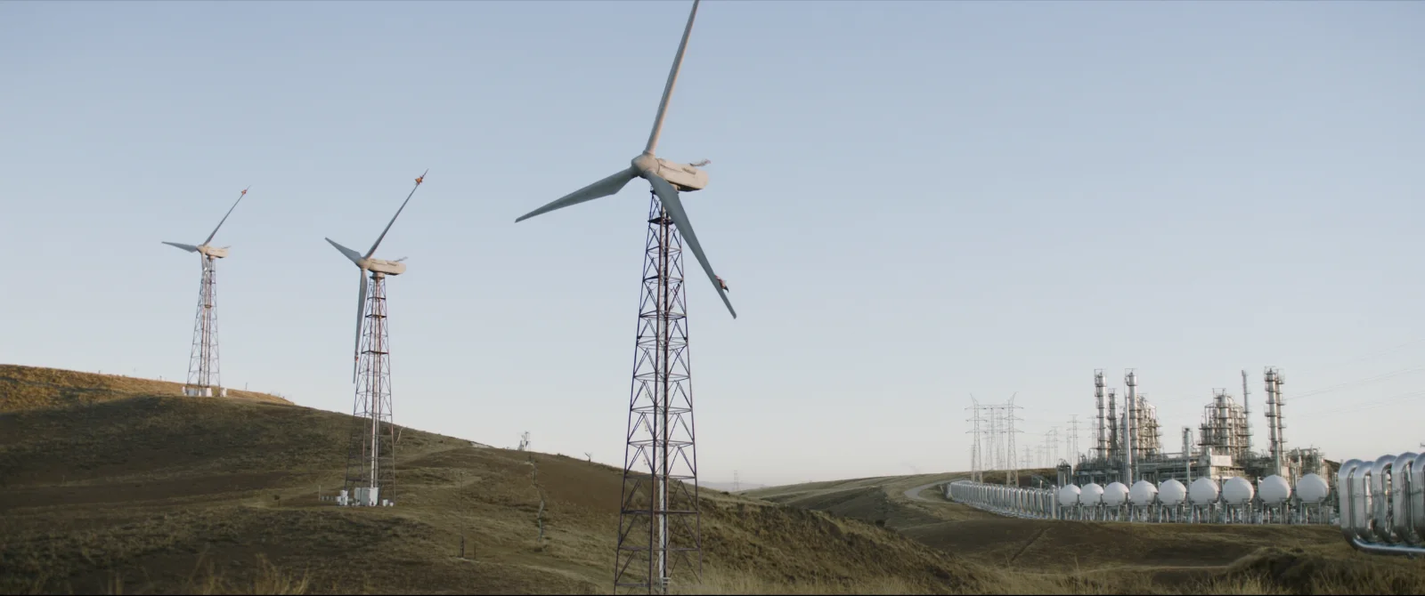 Aerogeneradores en colinas y una planta de procesamiento de gas natural con torres de transmisión al fondo